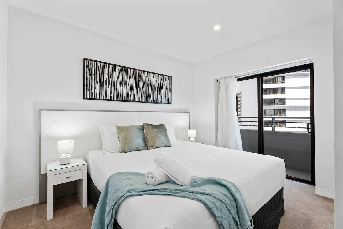 Un dormitorio luminoso con una cama tendida y una ventana grande.