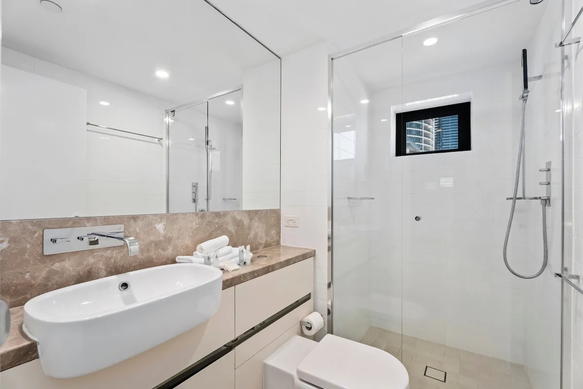 Un baño luminoso con lavabo, espejo amplio y ducha de vidrio.