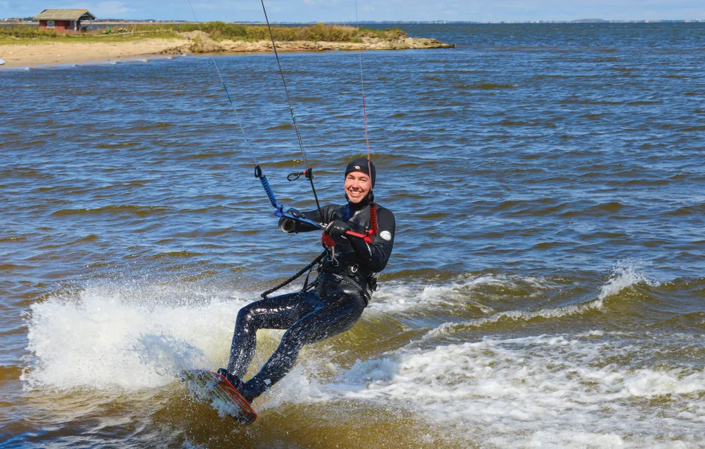 Una persona practica kitesurf sobre aguas agitadas cerca de una orilla arenosa.