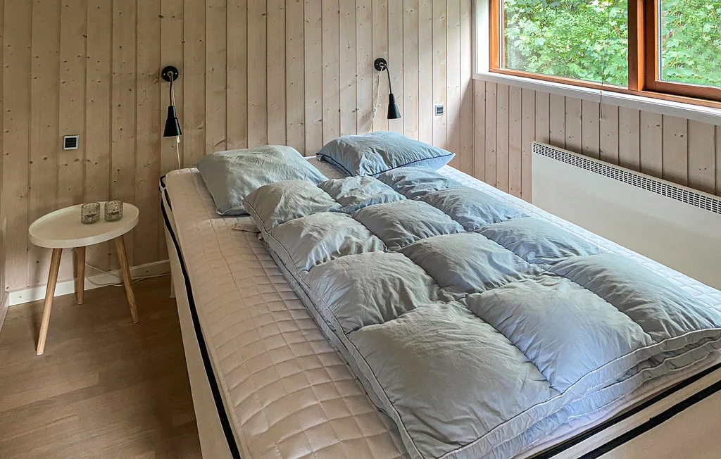Un dormitorio con una cama cubierta con ropa de cama gris junto a una ventana.