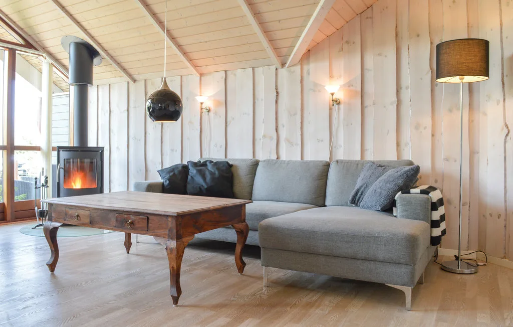 Una sala de estar con asientos grises, una mesa de centro de madera y una chimenea encendida.