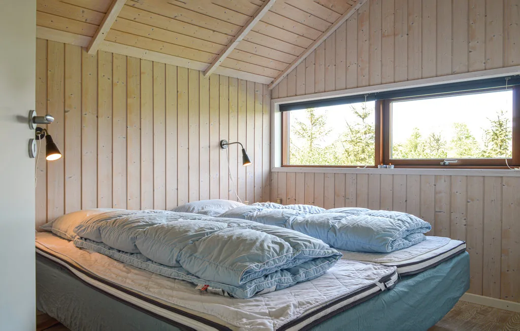 Un dormitorio con una cama grande bajo un techo inclinado de madera y una ventana amplia.