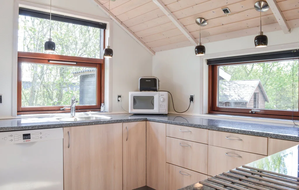 Una cocina luminosa con gabinetes de madera clara, encimera y ventanas con vista a los árboles.