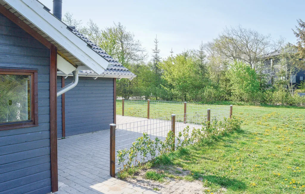 Una casa pequeña da a un patio pavimentado junto a un jardín con césped.