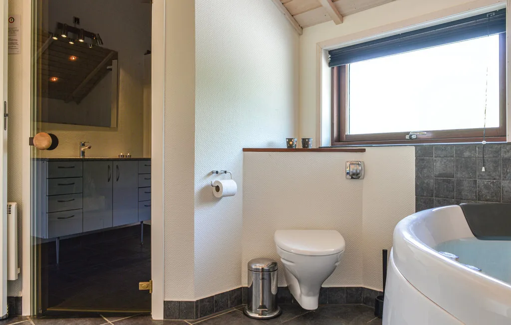 Un baño con inodoro, lavabo y bañera curva bajo una ventana amplia.