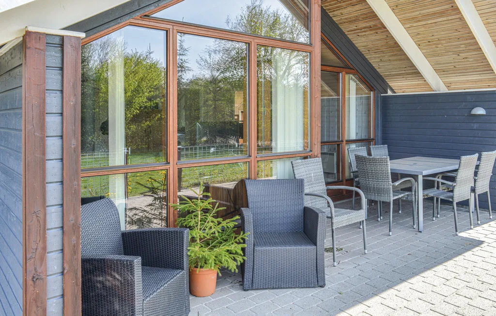 Una zona de estar exterior cubierta con sillas y una mesa junto a grandes ventanas.