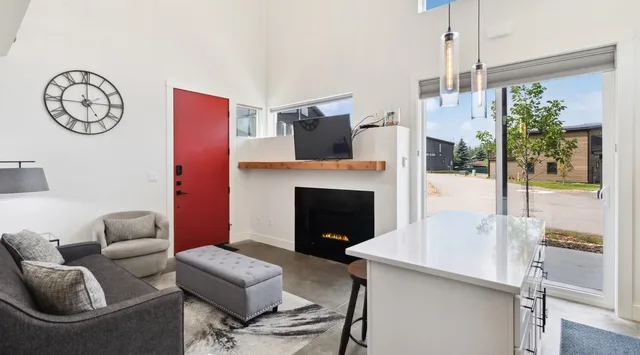 Una sala luminosa con asientos, chimenea y una isla grande junto a puertas de vidrio.