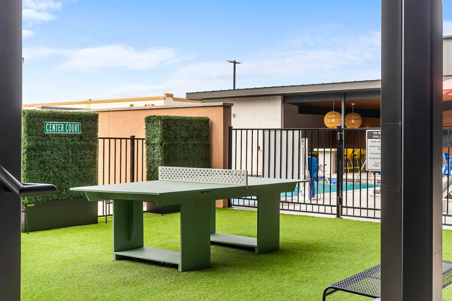 Zona recreativa al aire libre con una mesa de ping-pong verde sobre césped artificial junto a una piscina cercada.