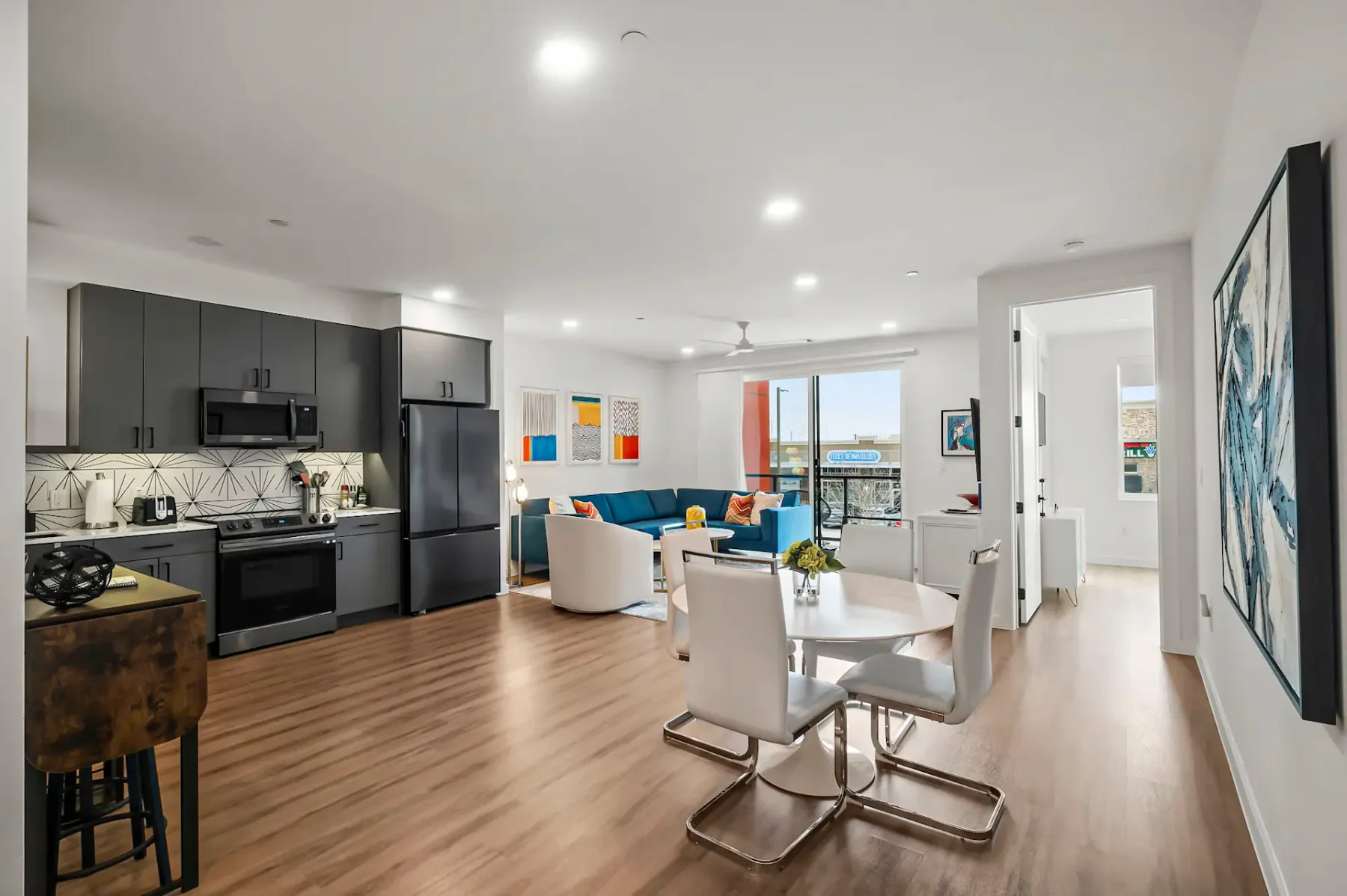 Apartamento moderno de planta abierta con cocina, comedor y sala de estar. Decoración luminosa, pisos de madera y arte en las paredes. Se aprecia una vista del balcón.