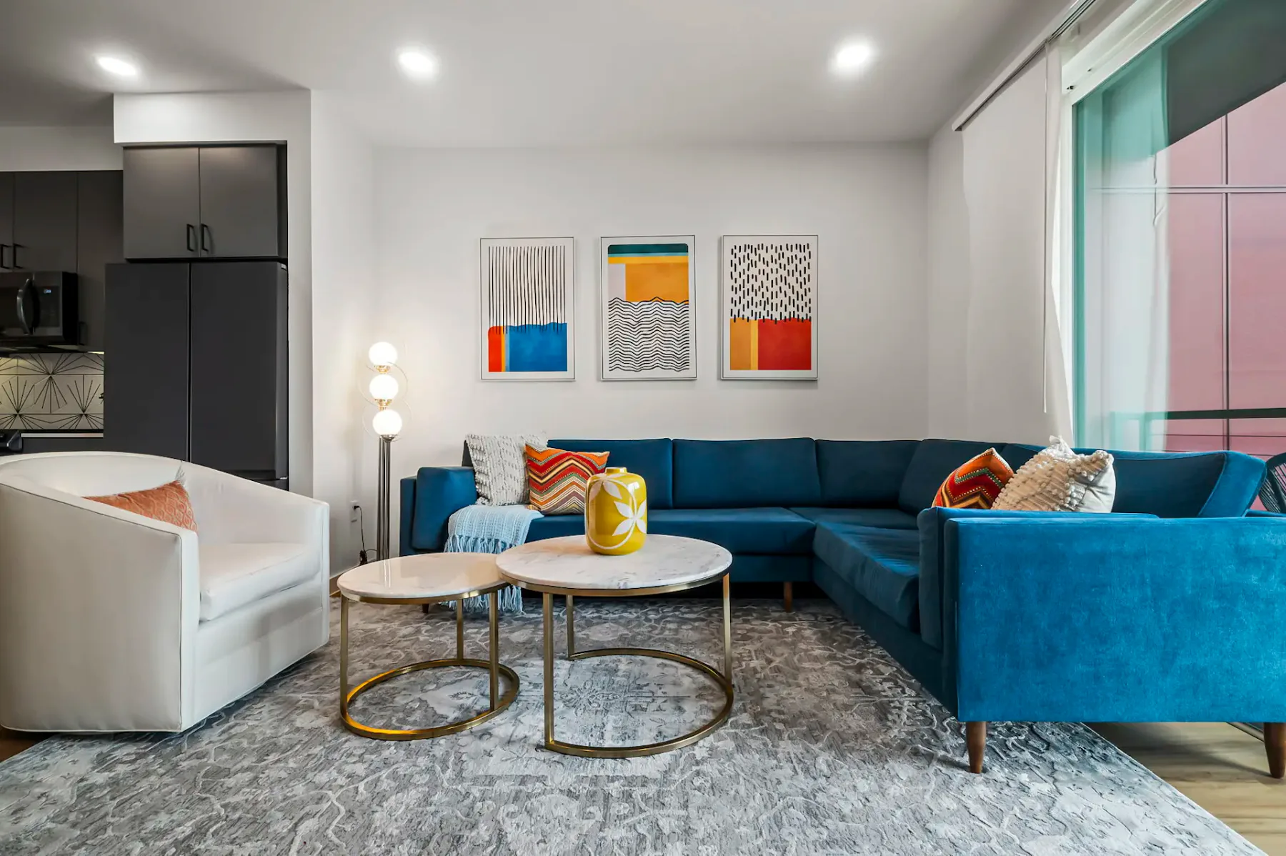 Una sala de estar con asientos azules, cuadros y una ventana grande.