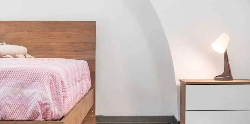 A bedroom with a bed beside a small table and lit lamp.