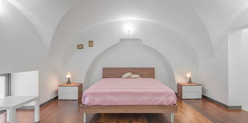 A bedroom with a bed covered in pink bedding beneath a curved white ceiling.