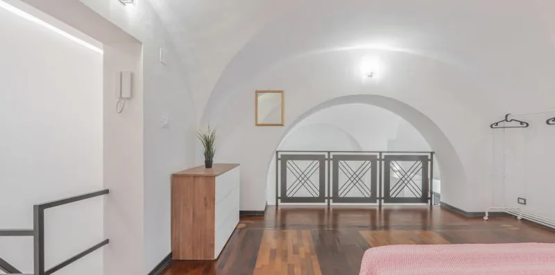 A bright bedroom with a wooden dresser and a metal bed frame beneath an arched ceiling.