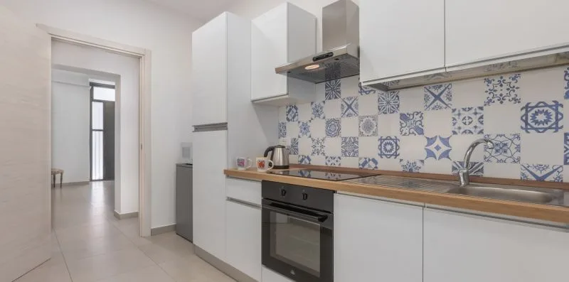 A modern kitchen with white cabinetry, a tiled backsplash, and an oven.