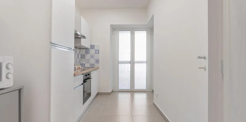 A narrow kitchen with a tiled backsplash and glass doors at the far end.