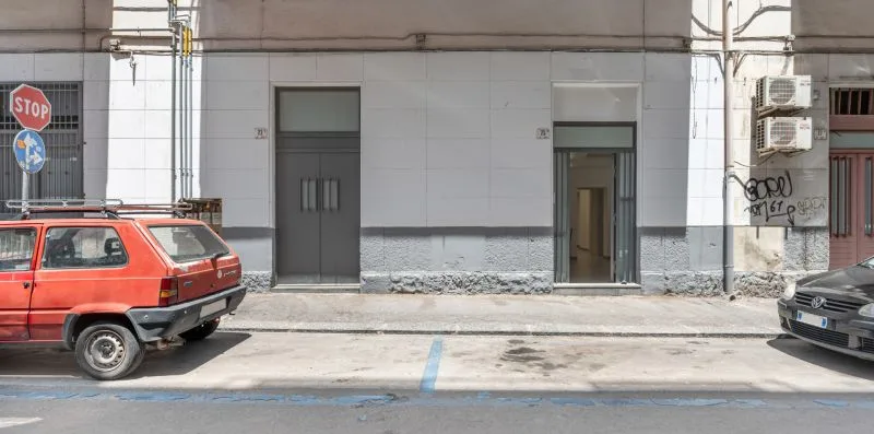 A street scene with a red car parked beside a gray building.