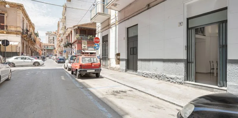 A narrow urban street lined with buildings and parked cars.