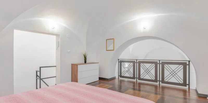 A bedroom with a pink bedspread, dresser, and arched railing.
