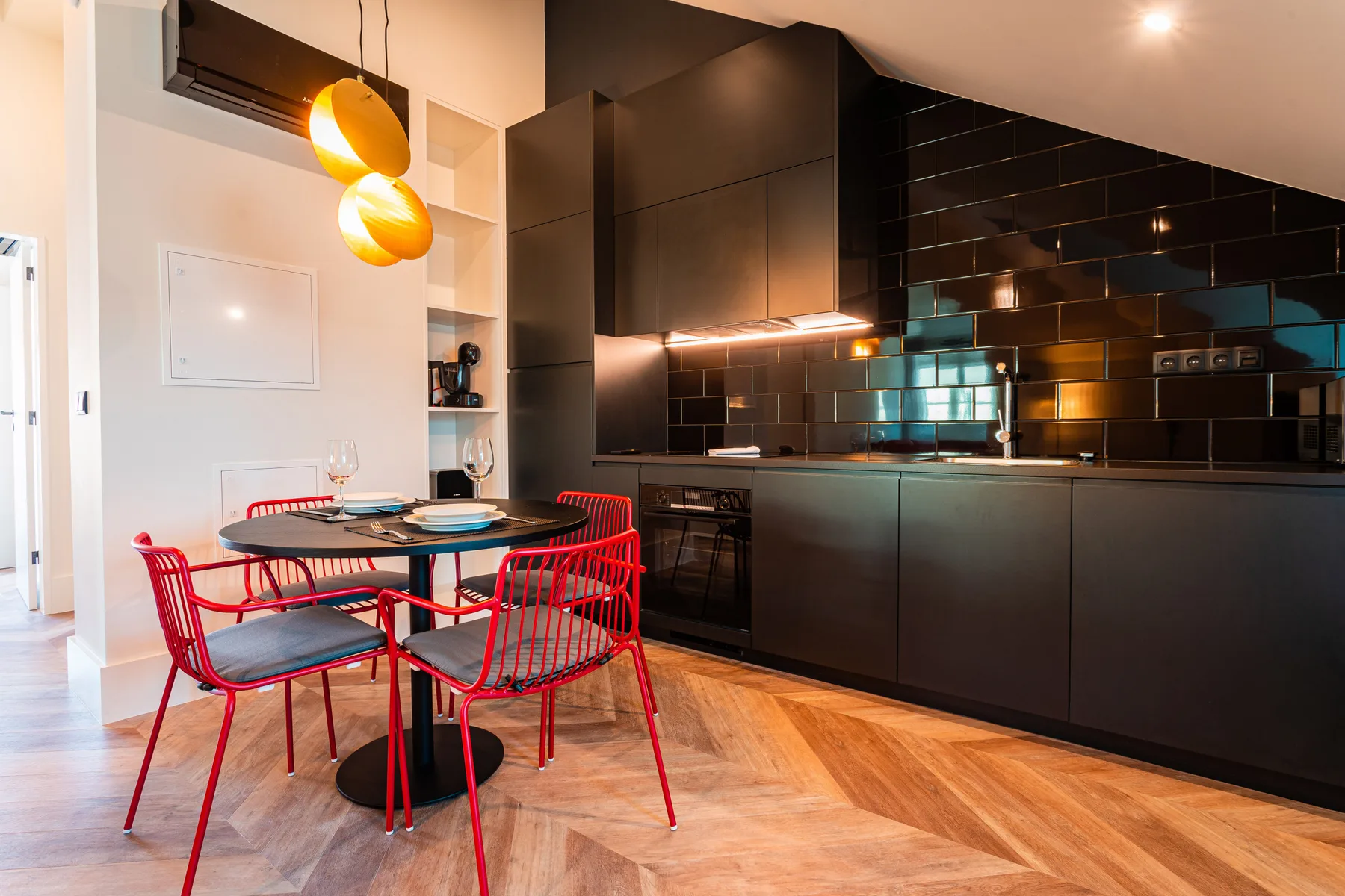Cocina y comedor modernos con armarios negros y asientos rojos.