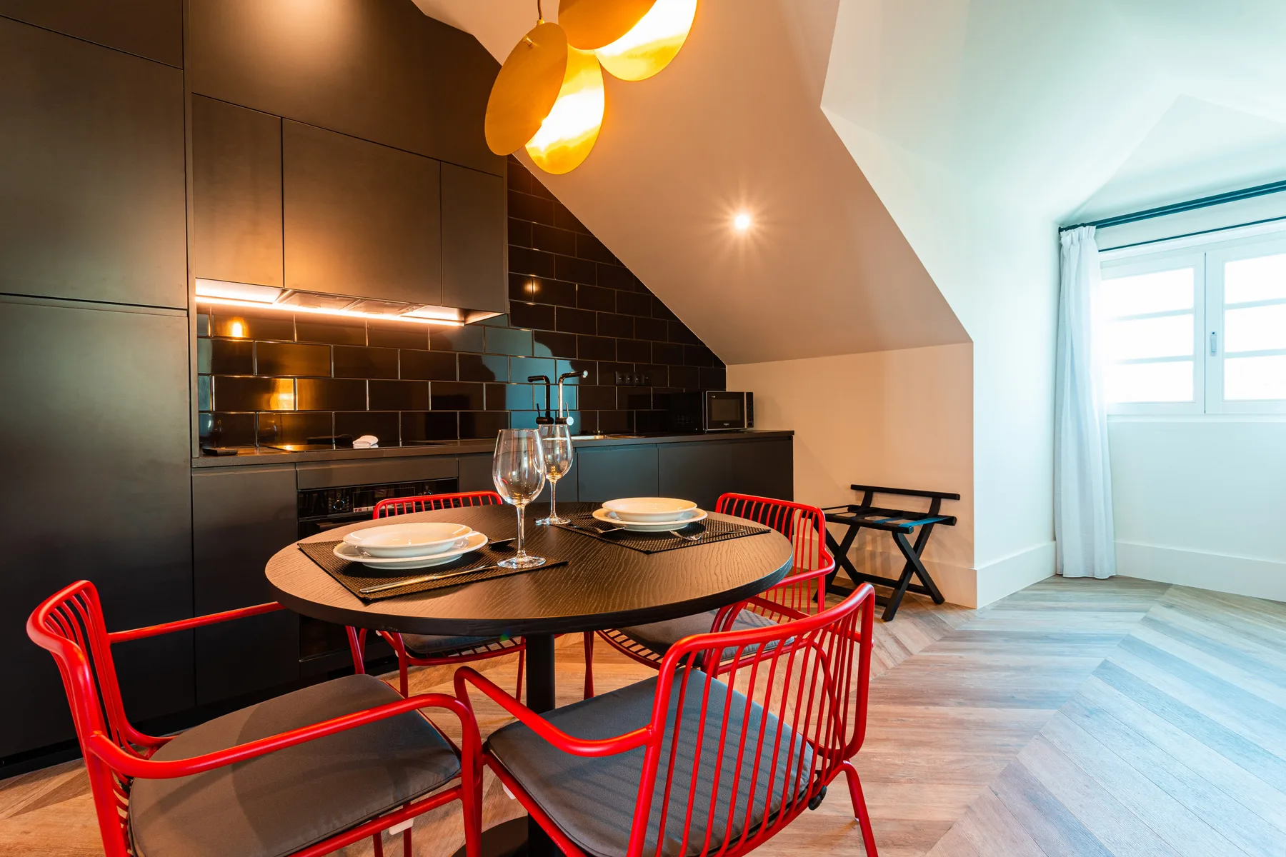 A dining area with a round table and red seating beside a dark kitchen.