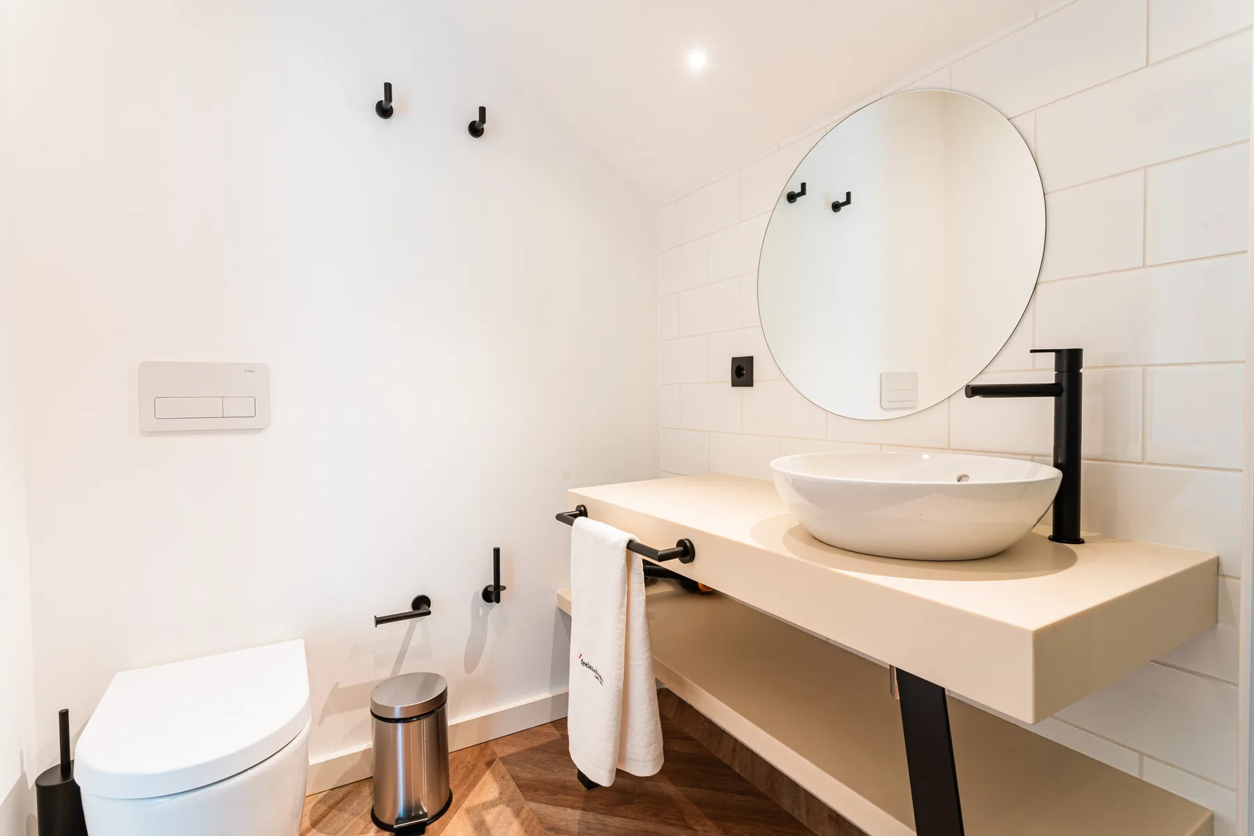 A modern bathroom with a sink, round mirror, and toilet.
