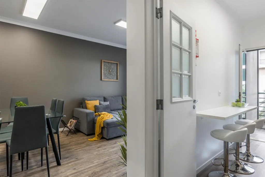 An open-plan living and dining area beside a kitchen counter with bar stools.