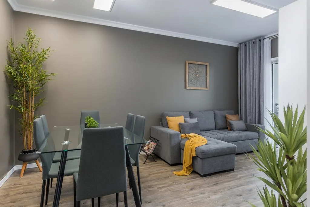 A living and dining area with gray seating, a glass table, and tall plants.
