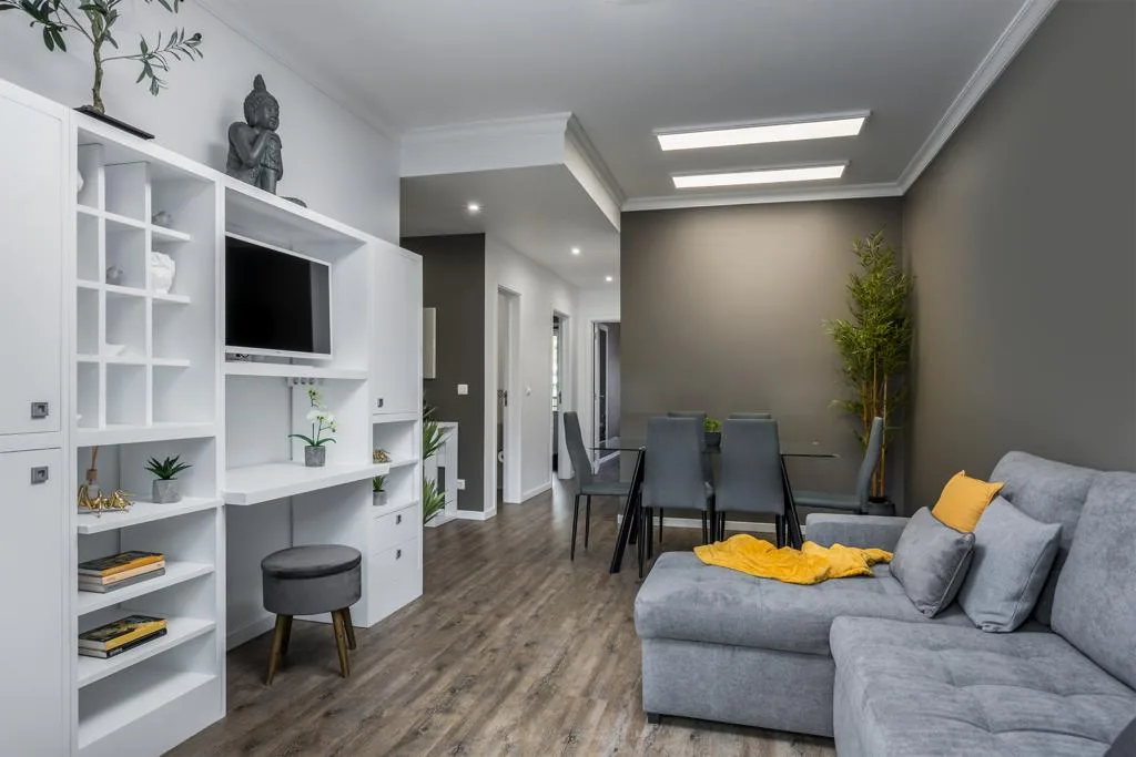 A modern living room with gray seating, built-in shelves, and a dining area.
