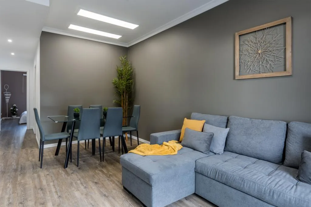 A living and dining area with blue seating and a table beneath framed wall art.