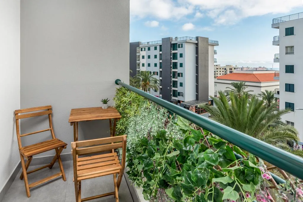 A balcony with wooden seating overlooks greenery and nearby buildings.