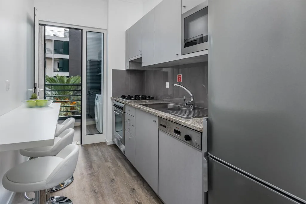 A compact kitchen with a counter, cooktop, and dining seating by the window.