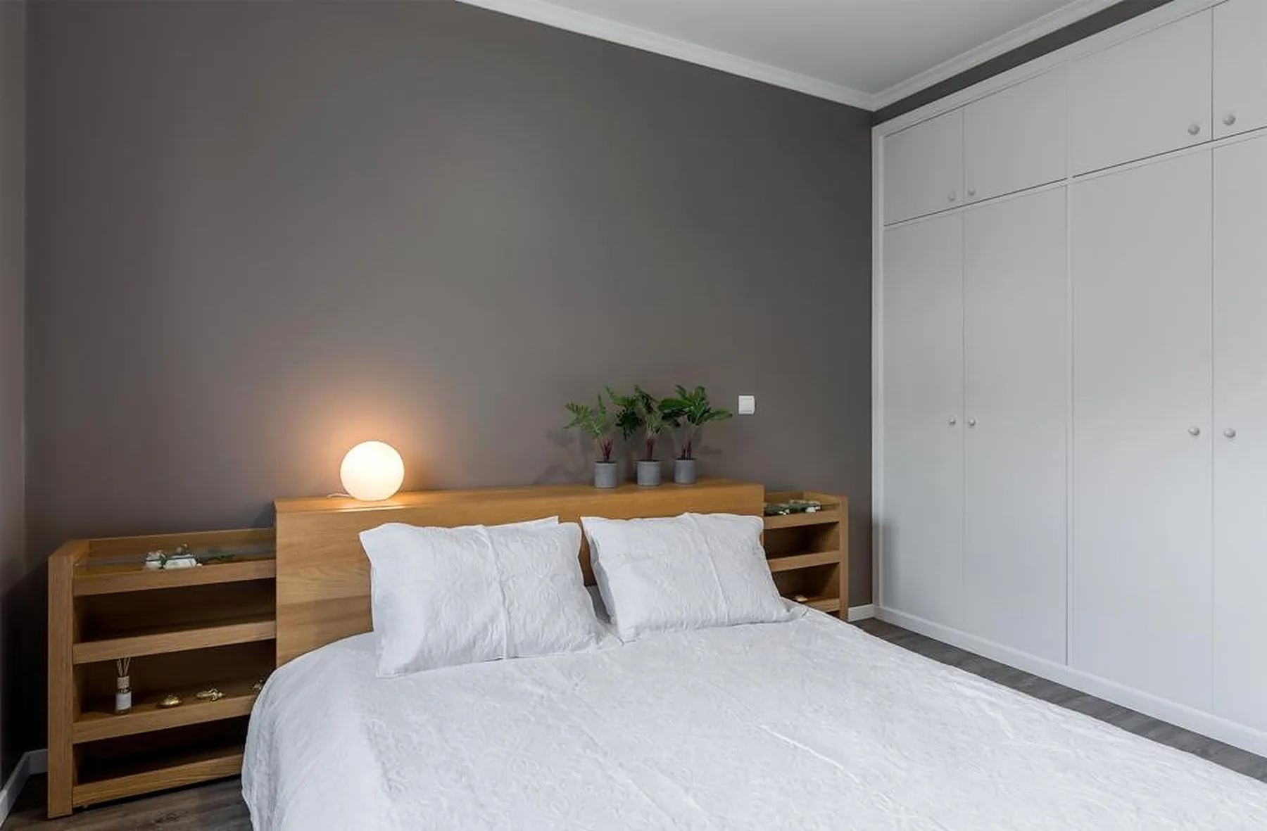 A bedroom with a neatly made bed, bedside shelving, and built-in cupboards.