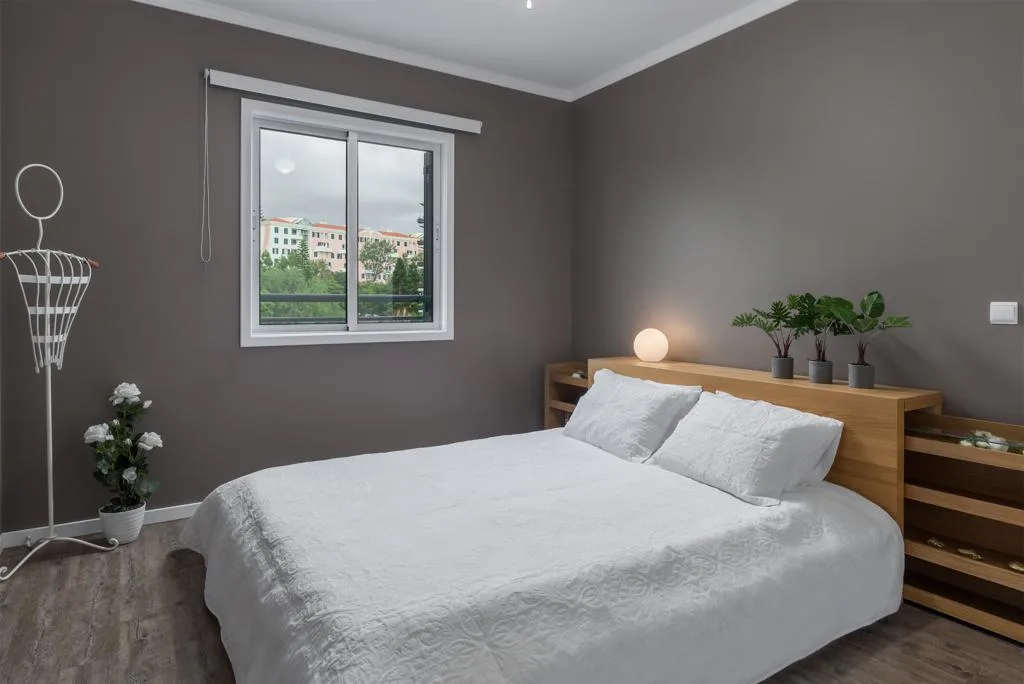 A bedroom with a neatly made bed beside a window.