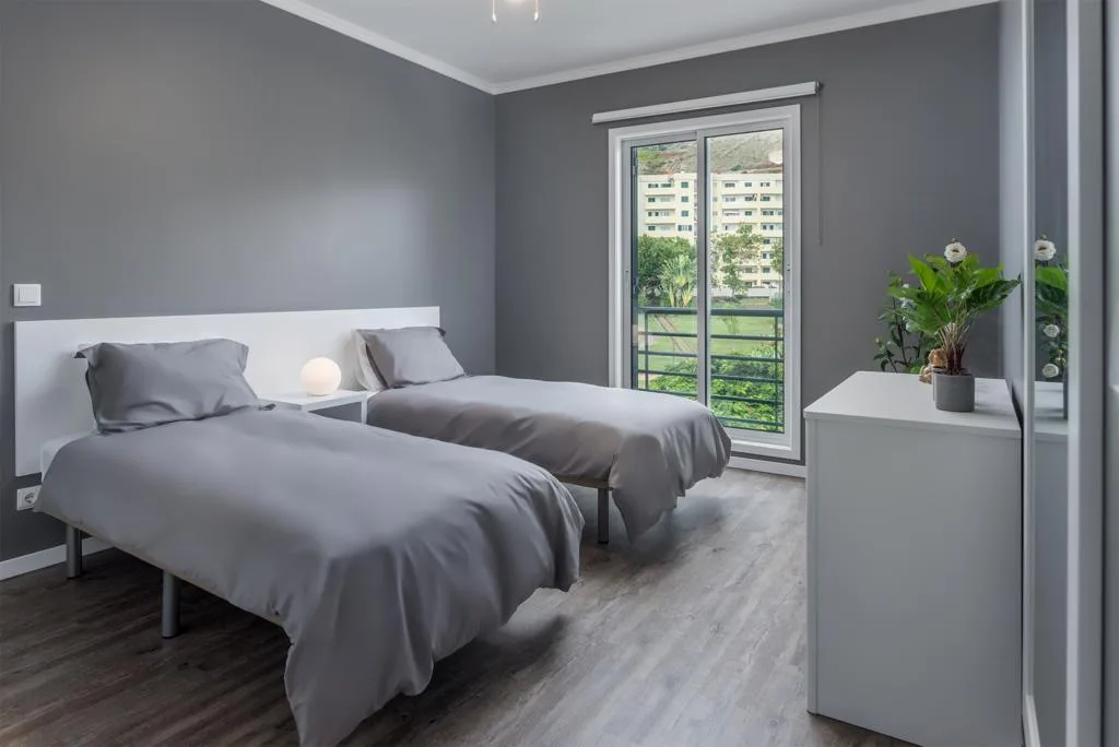 A bedroom with two beds and a sliding glass door opening onto a balcony.