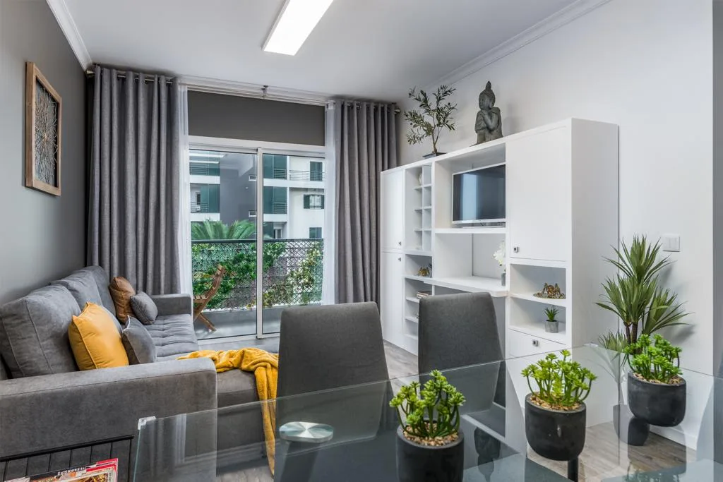 A living room with gray seating, a glass table, and large windows.