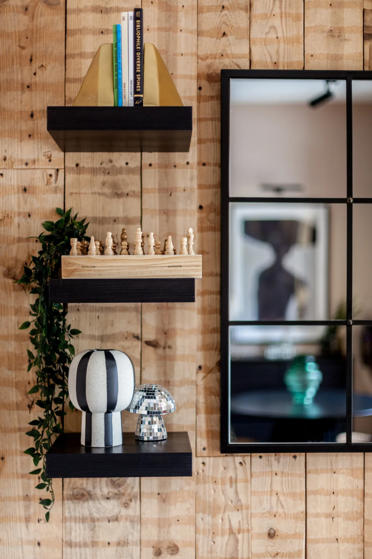 A decorated wooden wall features floating shelves, plants, and framed artwork.