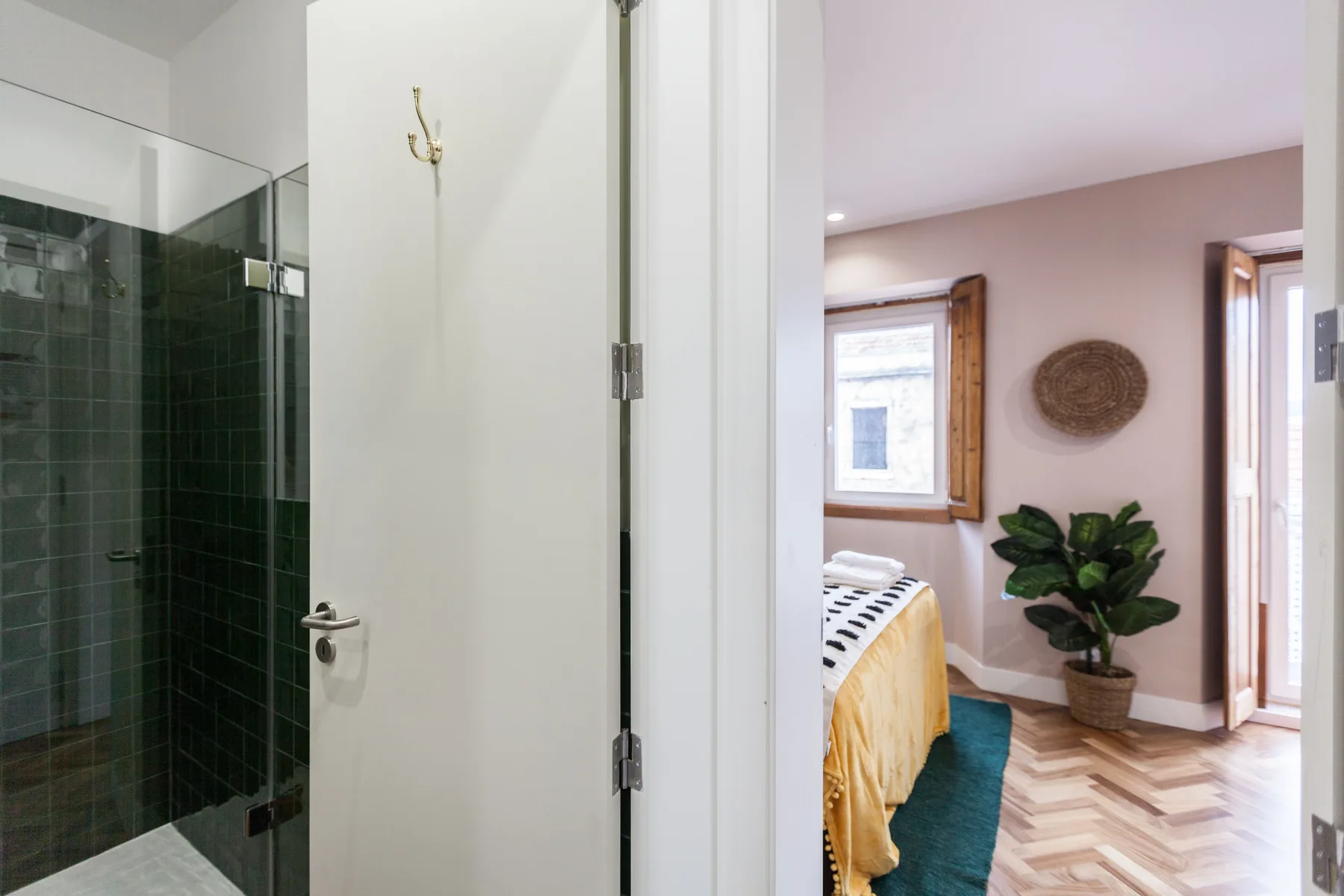 A bedroom with a bed, leafy plant, and doorway to a glass shower.