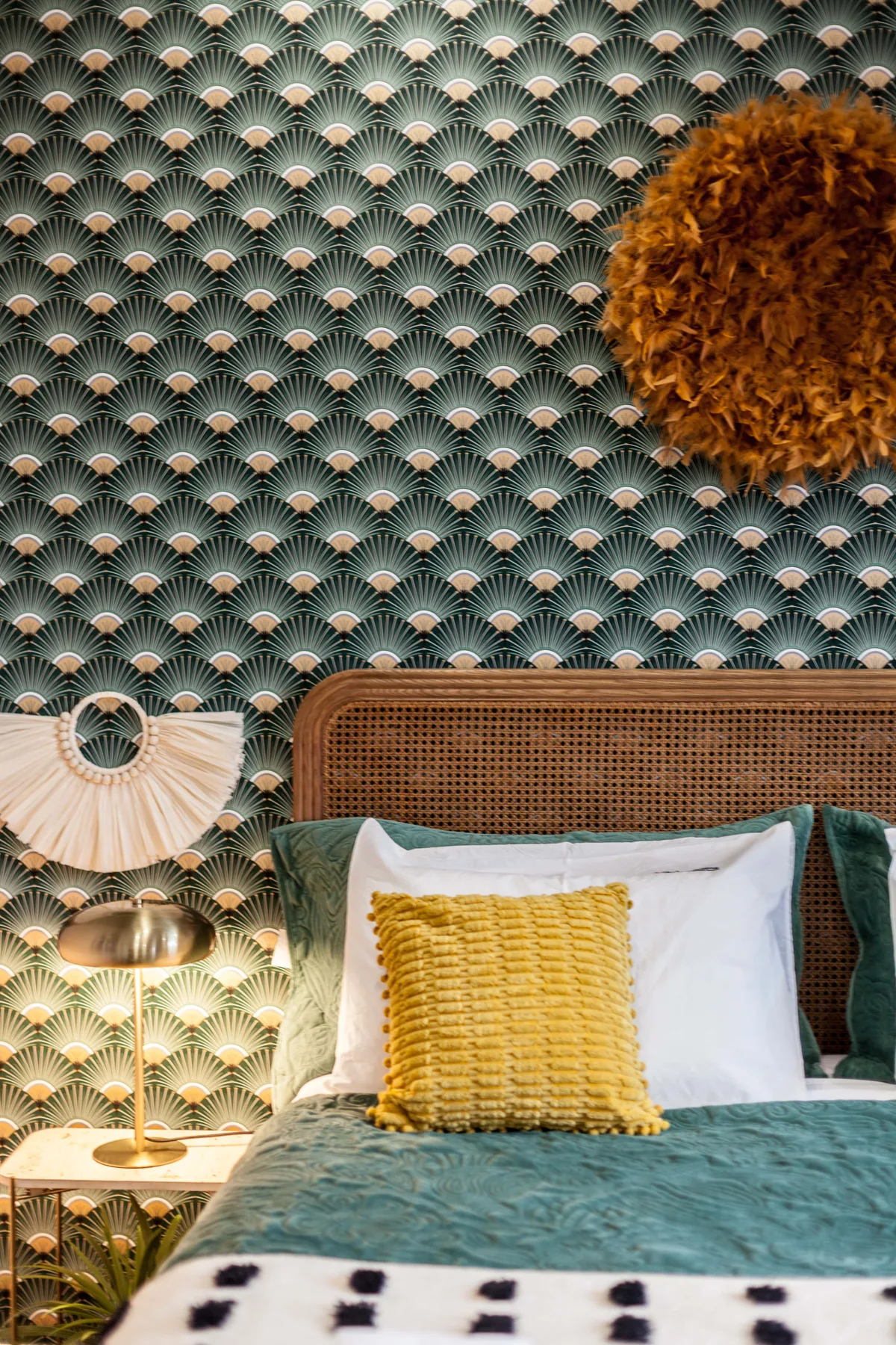 A bedroom with a patterned wall, layered pillows, and a bedside lamp.