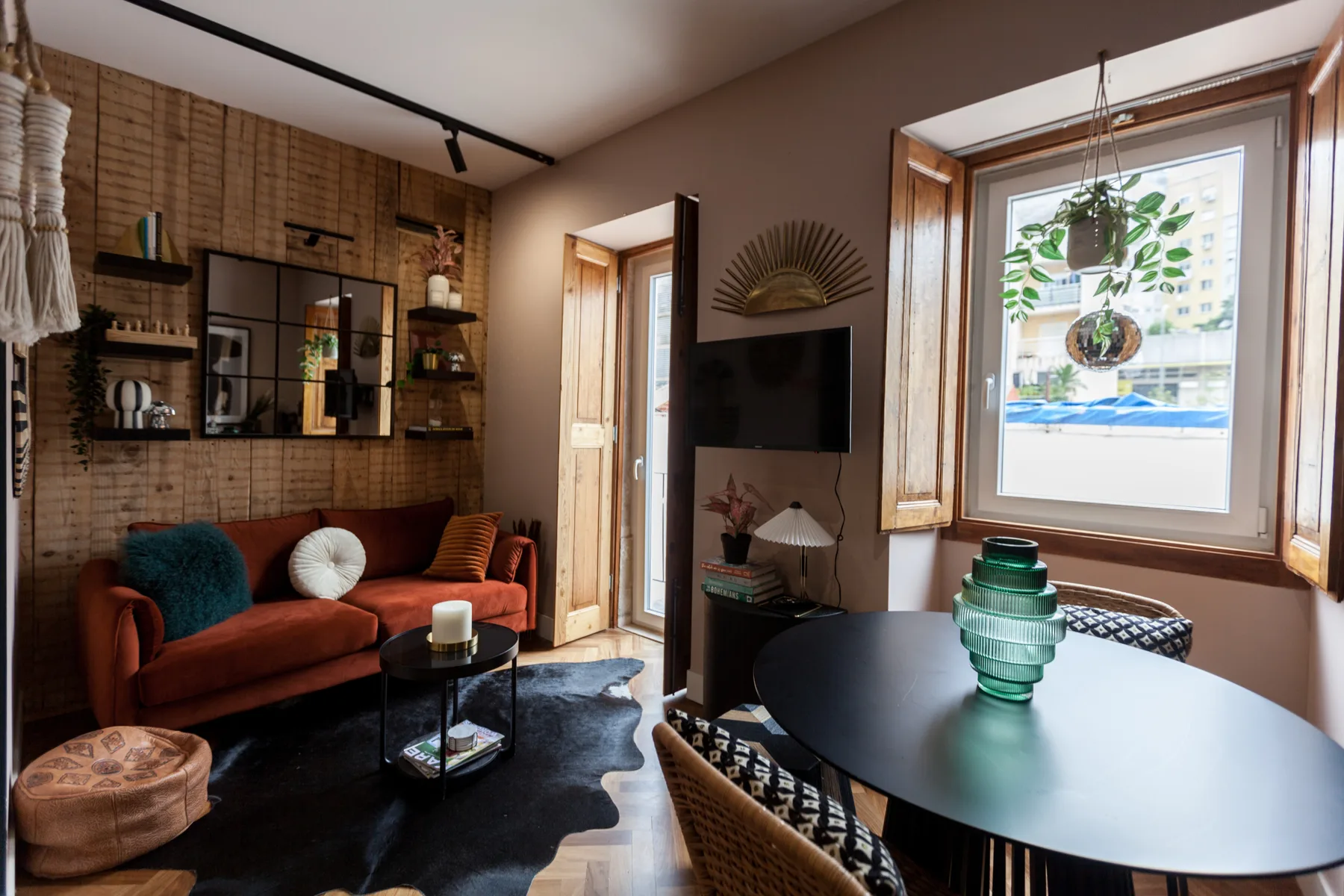 A living room with a rust-colored sofa, wall-mounted television, and dining table.