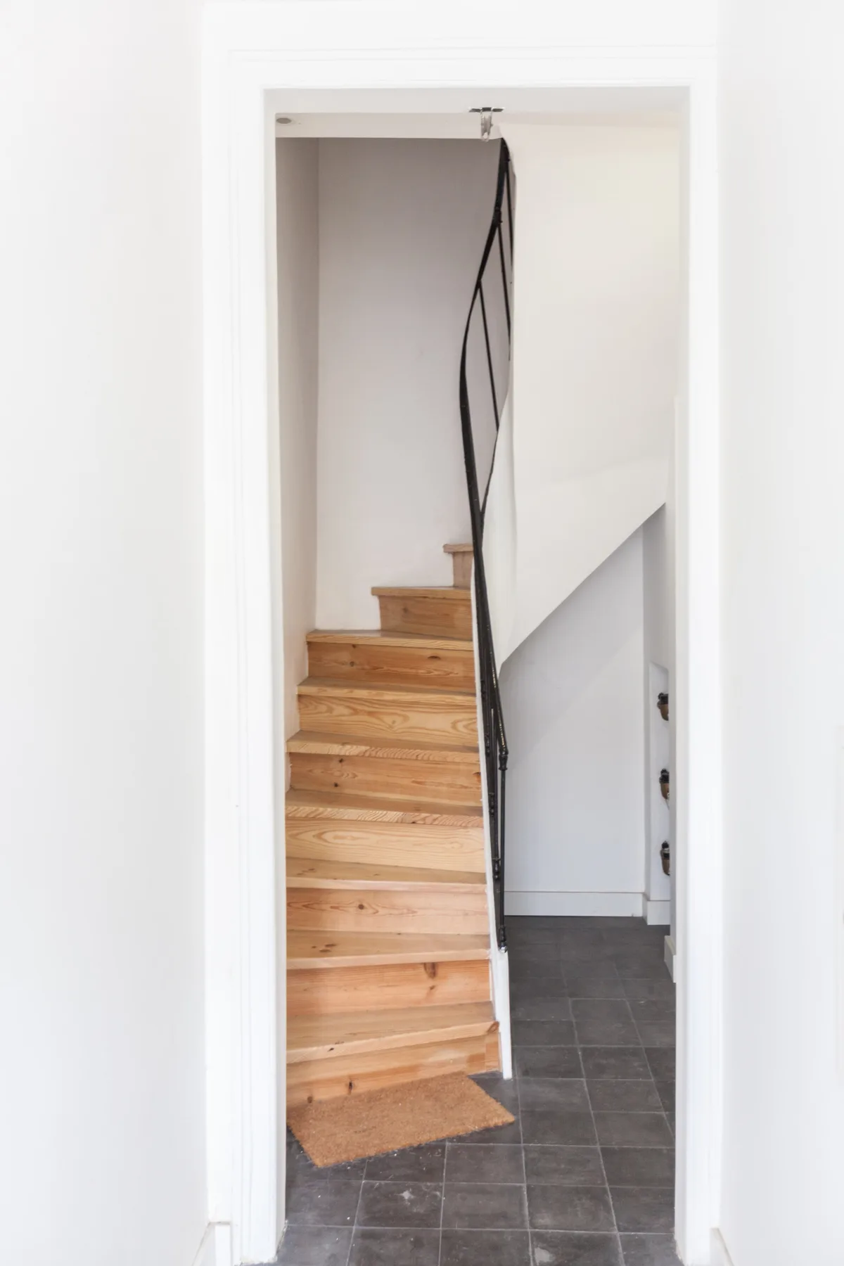 A narrow indoor stairway with wooden steps and a dark tiled floor.