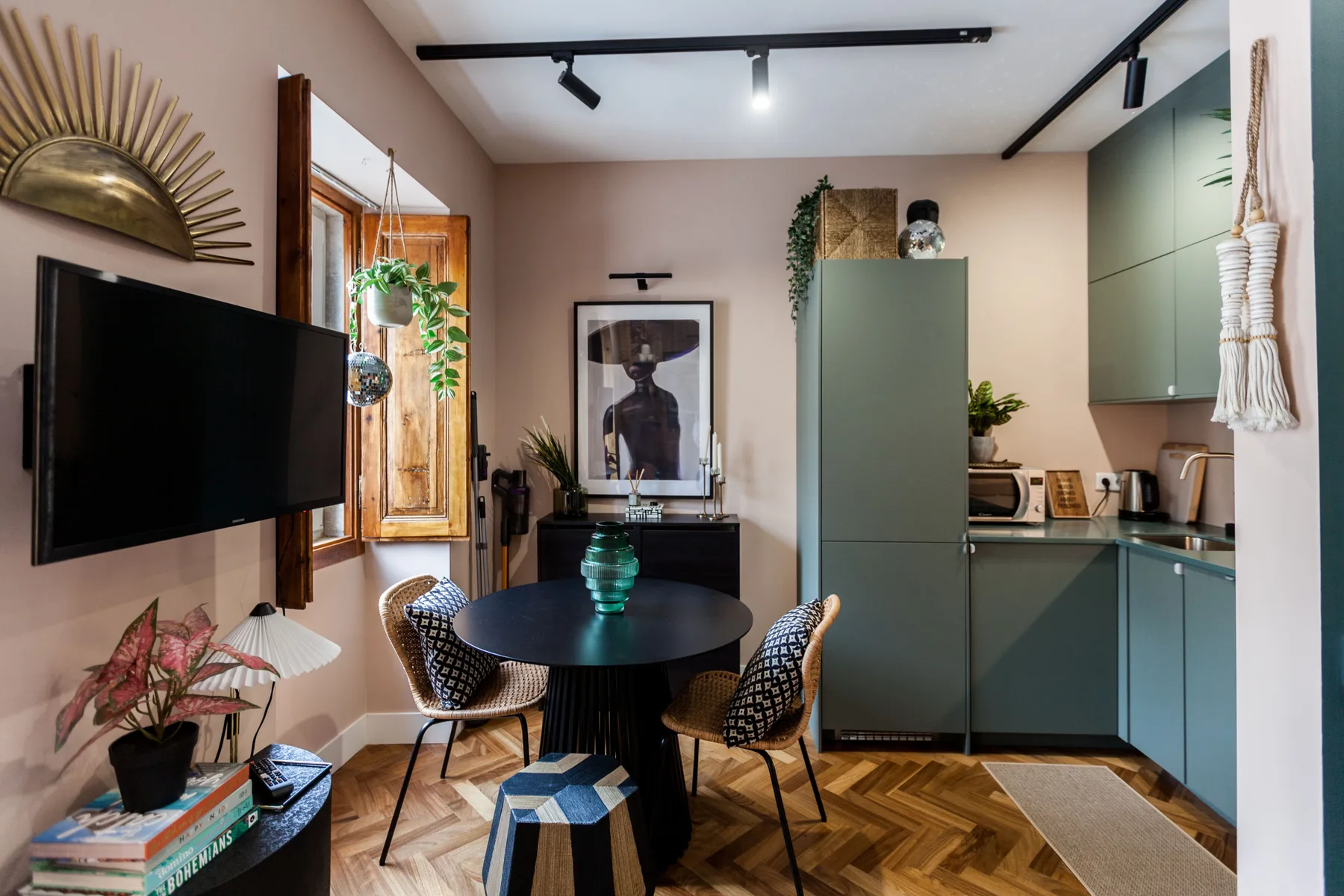 A dining area beside a compact kitchen, with a round table and woven seating.