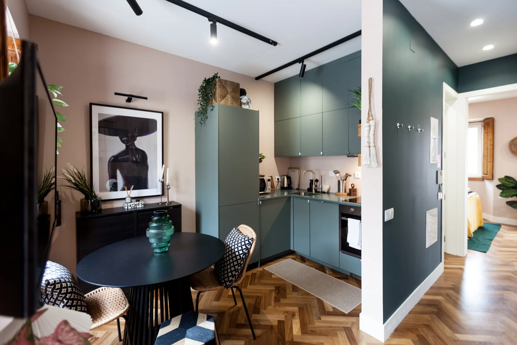 A dining area opens onto a kitchen with green cabinets and a round table.