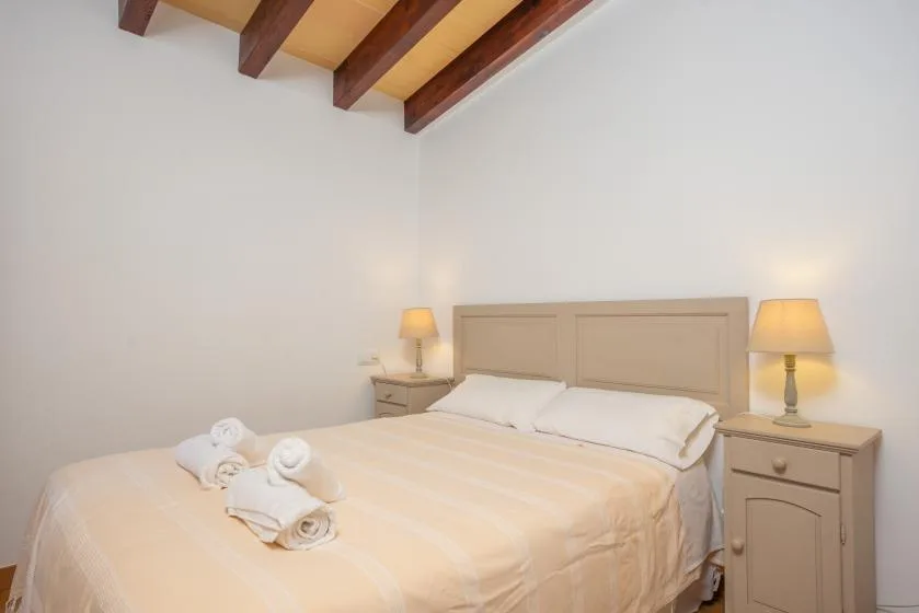 A bedroom with a bed and matching bedside tables beneath exposed ceiling beams.