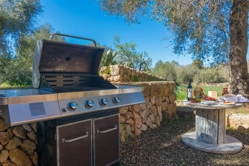An outdoor barbecue grill stands beside a stone wall and a small table.