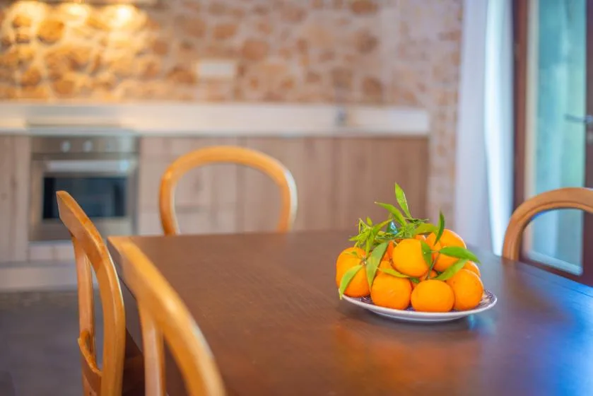 A dining table with a plate of oranges sits in a kitchen.