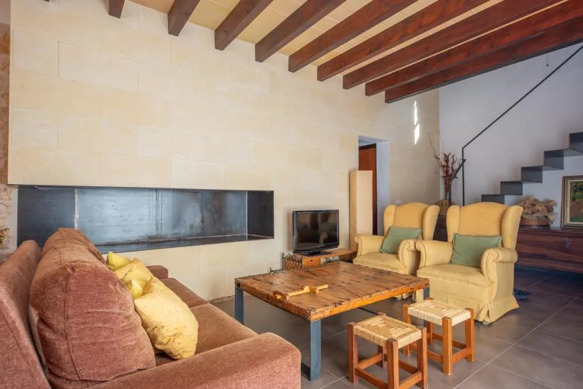 A living room with seating around a wooden coffee table beneath exposed ceiling beams.