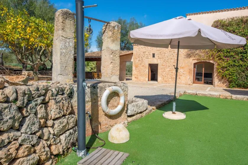 A sunny outdoor patio has a large umbrella beside a stone building.