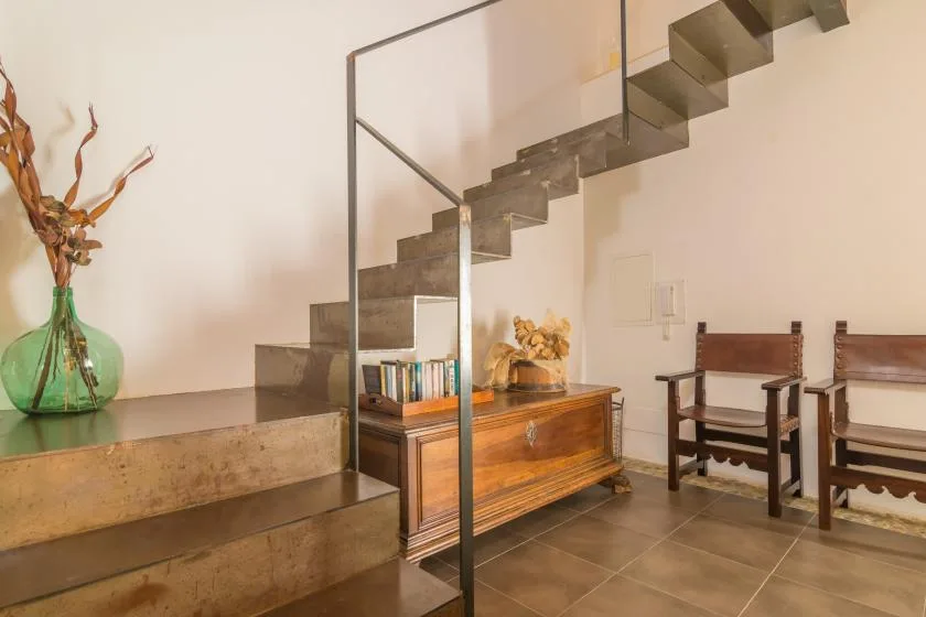 A furnished interior with a staircase, wooden chest, and seating.