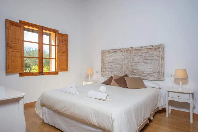 A bright bedroom with a double bed beneath a pale wall hanging.