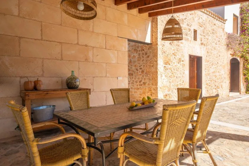 An outdoor dining area with a table and woven seating beneath a covered terrace.
